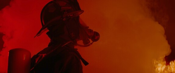 Dramatic silhouette of American firefighter in full gear exploring the huge fire zone
