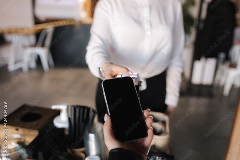 First person view of human hand hold smart phone for payment by NFC at the cafe. Closeup of female hand that giving terminal for online payment First person view of human hand hold smart phone for payment by NFC at the cafe. Closeup of female hand that giving terminal for online payment