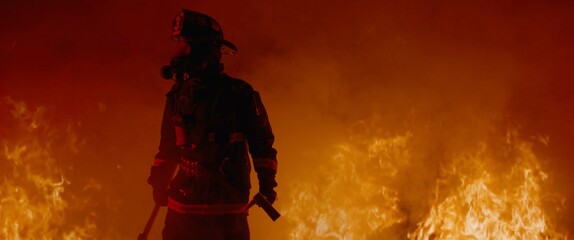Dramatic silhouette of American firefighter in full gear exploring the huge fire zone