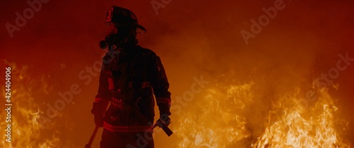 Slika na platnu Dramatic silhouette of American firefighter in full gear exploring the huge fire