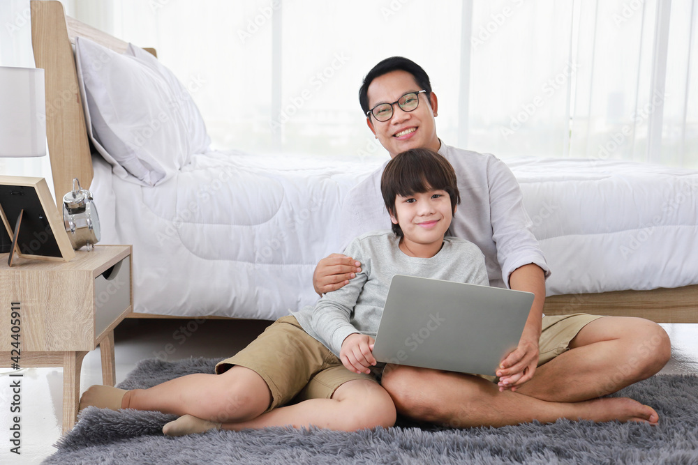 Asian father teaching homework to his son in bedroom while looking at camera for homeschooling, distance learning and education concept Asian father teaching homework to his son in bedroom while looking at camera for homeschooling, distance learning and education concept