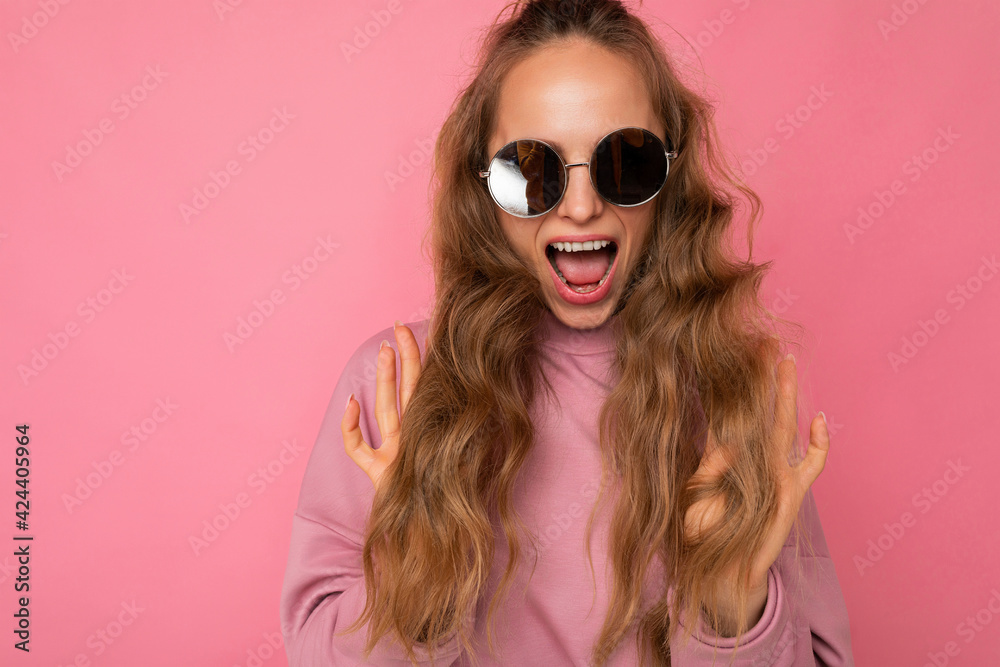 Shot of beautiful surprised happy young dark blonde curly woman isolated over pink background wall wearing casual pink sport clothes and stylish sunglasses looking at camera and shouting Shot of beautiful surprised happy young dark blonde curly woman isolated over pink background wall wearing casual pink sport clothes and stylish sunglasses looking at camera and shouting