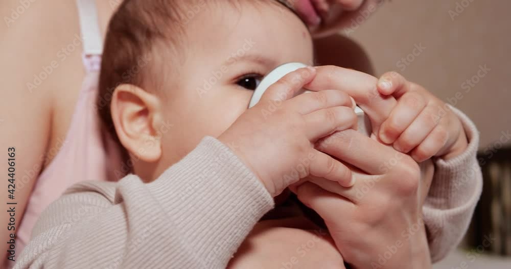 Portrait of a little boy who sits in his mother's arms. Happy child drinks milk or dairy product from a cup. Proper and natural nutrition for children