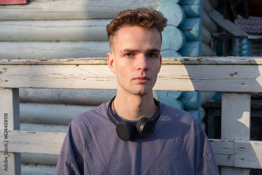Portrait of a handsome guy with a tattoo on his arm, wearing headphones on the background of a blue wooden wall on the street