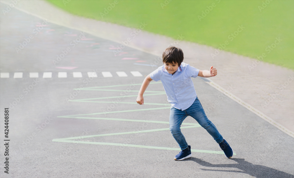Full length portrait of young boy running or jumping on triangles line at asphalt road, Active kid playing in the public park on sunny day spring or summer, Child play and learn outdoor activity