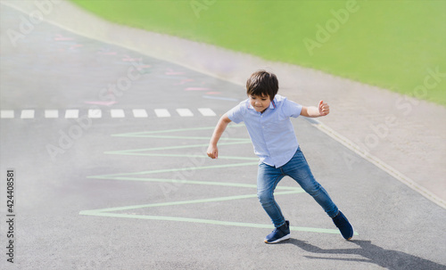 Full length portrait of young boy running or jumping on triangles line at asphalt road, Active kid playing in the public park on sunny day spring or summer, Child play and learn outdoor activity © Anchalee