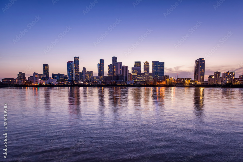 Wide panoramic view over the Thames river to the new skyline of the financial district Canary Wharf in London, United Kingdom, during dusk