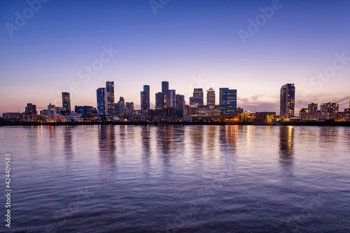 Wide panoramic view over the Thames river to the new skyline of the financial district Canary Wharf in London, United Kingdom, during dusk