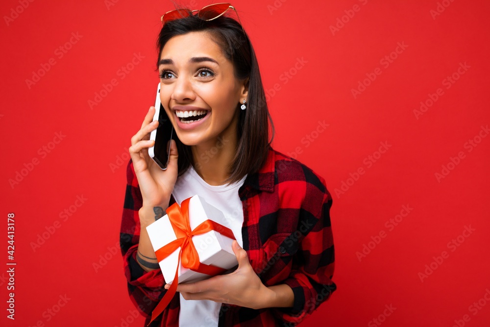 Beautiful happy young brunette woman isolated over colourful background wall wearing stylish casual clothes holding gift box and looking to the side Beautiful happy young brunette woman isolated over colourful background wall wearing stylish casual clothes holding gift box and looking to the side