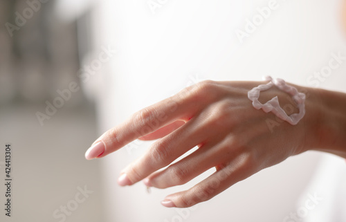 Hand cream on a woman's hand, heart shape. Young woman applying hand cream on grey background.