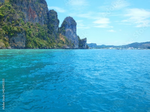 Tourist attraction of Thailand. Water excursions for tourists. Sea tour. Islands of the Phi Phi group, Phuket water area. Bright turquoise water, sheer cliff towering over the bay, boats and beach 
