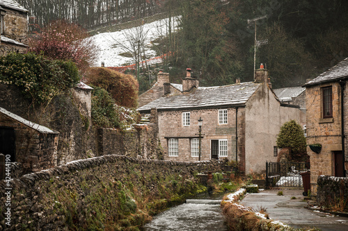 Castleton Hope Valley, Derbyshire Beautiful old rural idyllic village cottages in the Peak District river peacefully flowing during winter with snow on hills behind photo