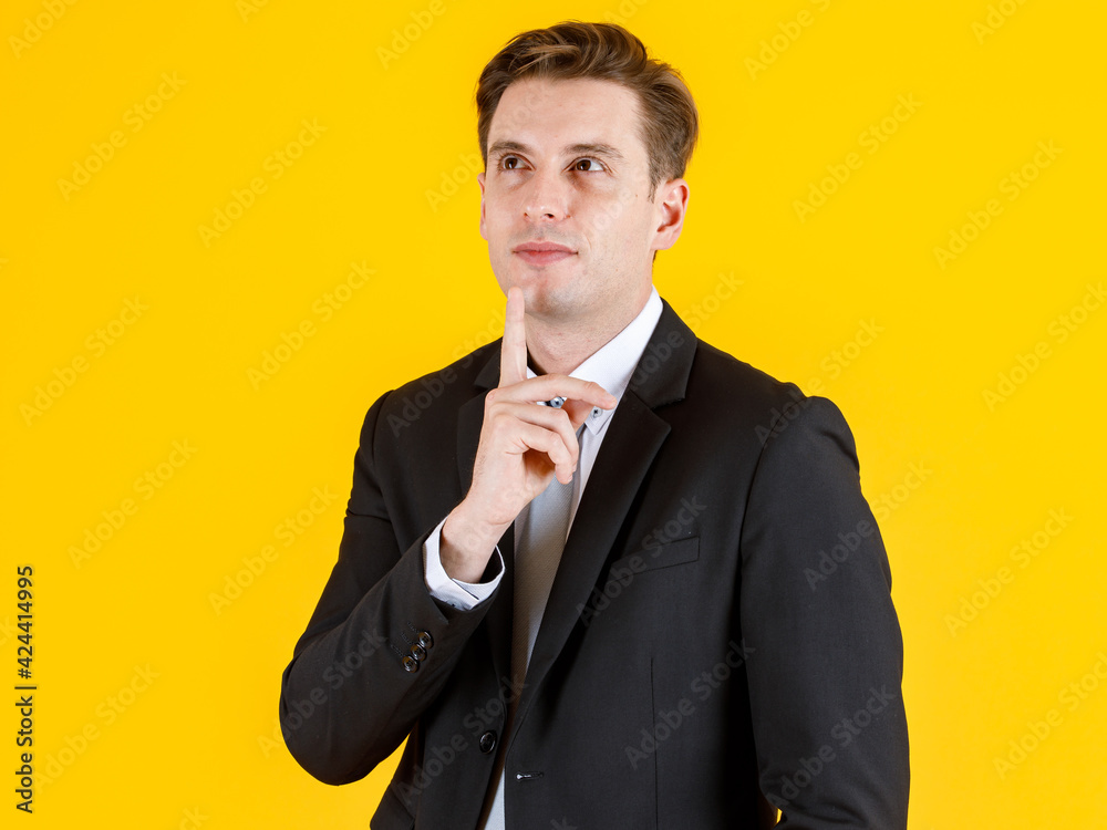 Portrait half body of handsome and executive look french businessman in black suit pointing finger to blank space in advertising pose. Successful and happy business man concept on yellow background Portrait half body of handsome and executive look french businessman in black suit pointing finger to blank space in advertising pose. Successful and happy business man concept on yellow background