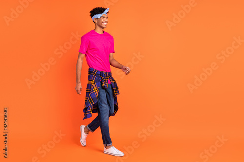 Full length body size photo young guy smiling walking forward in stylish outfit isolated vibrant orange color background