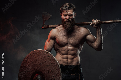 Frenzied viking in dark background with axe and shield