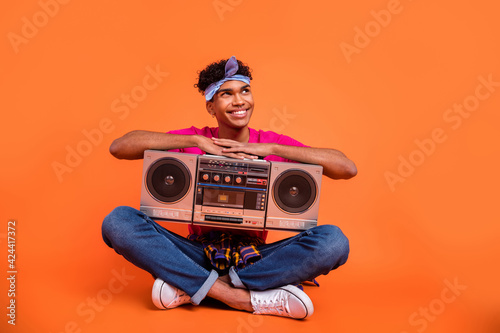 Full length body size photo of curious dreamy guy with tape recorder looking empty space isolated vibrant orange color background