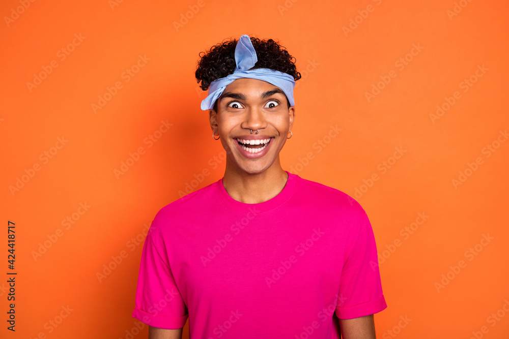 Photo portrait of smiling crazy guy wearing headband piercing staring amazed laughing isolated vibrant orange color background