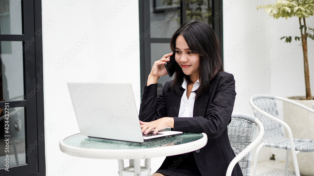 Asian young business woman working on computer and talking on smartphone in office Asian young business woman working on computer and talking on smartphone in office