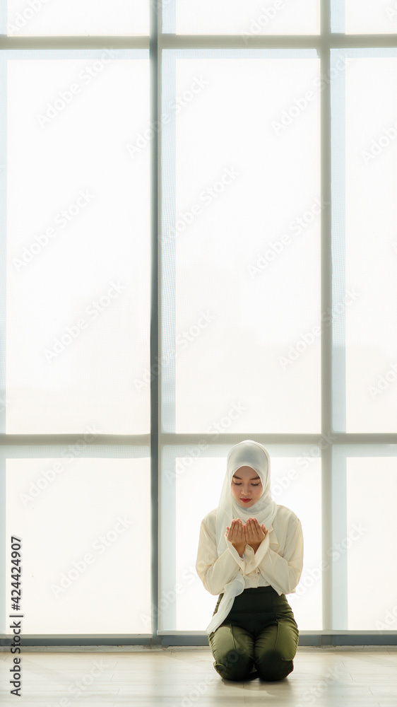 Young and beautiful Asian Muslim woman sitting on floor and praying with respect and calm manner Young and beautiful Asian Muslim woman sitting on floor and praying with respect and calm manner