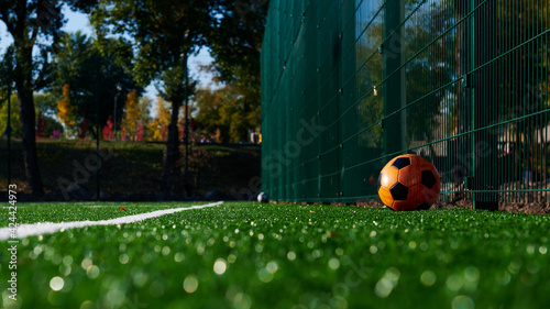 Artificial empty football field with an orange ball. Shallow depth of field. White line and copy space. Sunny day. Closeup. Wide web format photo.