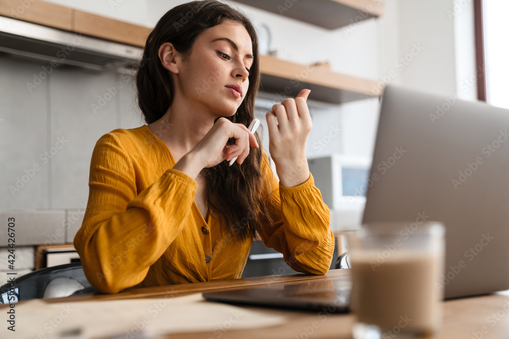Young european woman looking at her nails while working with laptop Young european woman looking at her nails while working with laptop