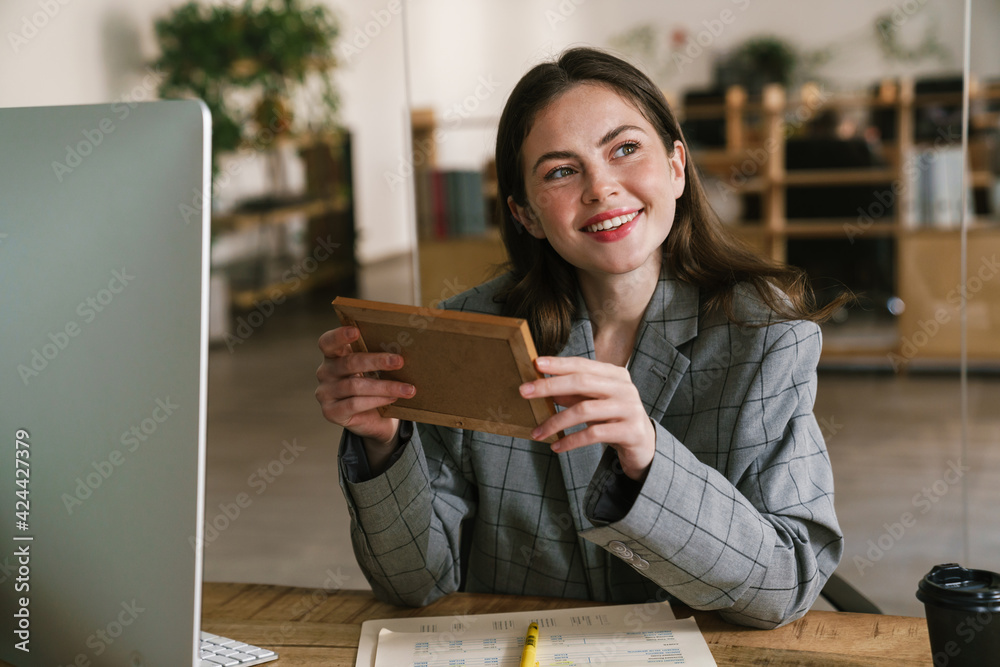 Young smiling woman looking at photo while working in office Young smiling woman looking at photo while working in office