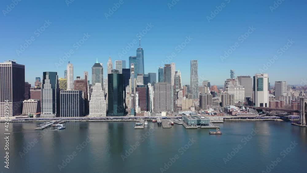 An aerial view over the east East River on a sunny day with blue skies. The drone camera, facing lower Manhattan truck left over the calm waters An aerial view over the east East River on a sunny day with blue skies. The drone camera, facing lower Manhattan truck left over the calm waters