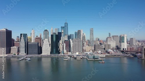 An aerial view over the east East River on a sunny day with blue skies. The drone camera, facing lower Manhattan truck left over the calm waters