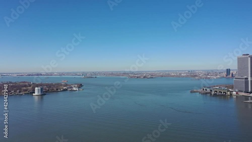 An aerial view the east East River on a sunny day with blue skies. The drone camera, facing lower Manhattan, pan left towards Governor's Island and Brooklyn Heights. photo