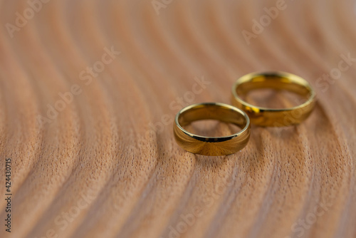 Two golden wedding rings close up on natural wooden background. Eco wedding invitation card concept. 