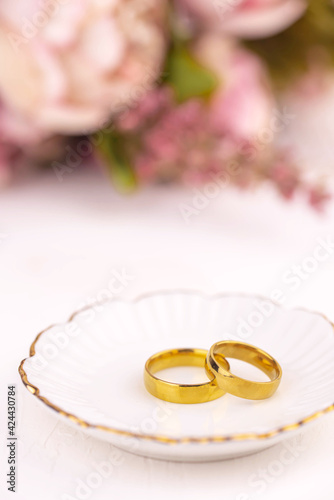 Two golden wedding rings close up with flowers on white background. Wedding invitation card concept. 