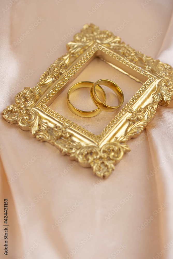 Two golden wedding rings close up with wooden picture frame on the cloth. Wedding invitation card concept. 