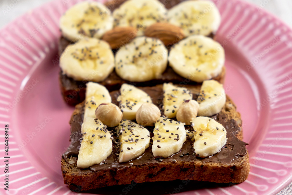 Toasted whole wheat bread with chocolate nuts paste nutella topping, banana, chia seeds, almonds and hazelnuts toast. Healthy proper nutrition for breakfast Toasted whole wheat bread with chocolate nuts paste nutella topping, banana, chia seeds, almonds and hazelnuts toast. Healthy proper nutrition for breakfast