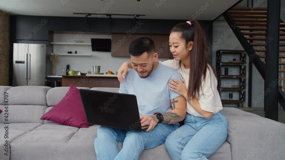 Loving carefree attractive asian couple relaxing and bracing on sofa, browsing social media content online using laptop pc, expressing positive vibes and happiness while enjoying leisure at home. Loving carefree attractive asian couple relaxing and bracing on sofa, browsing social media content online using laptop pc, expressing positive vibes and happiness while enjoying leisure at home.