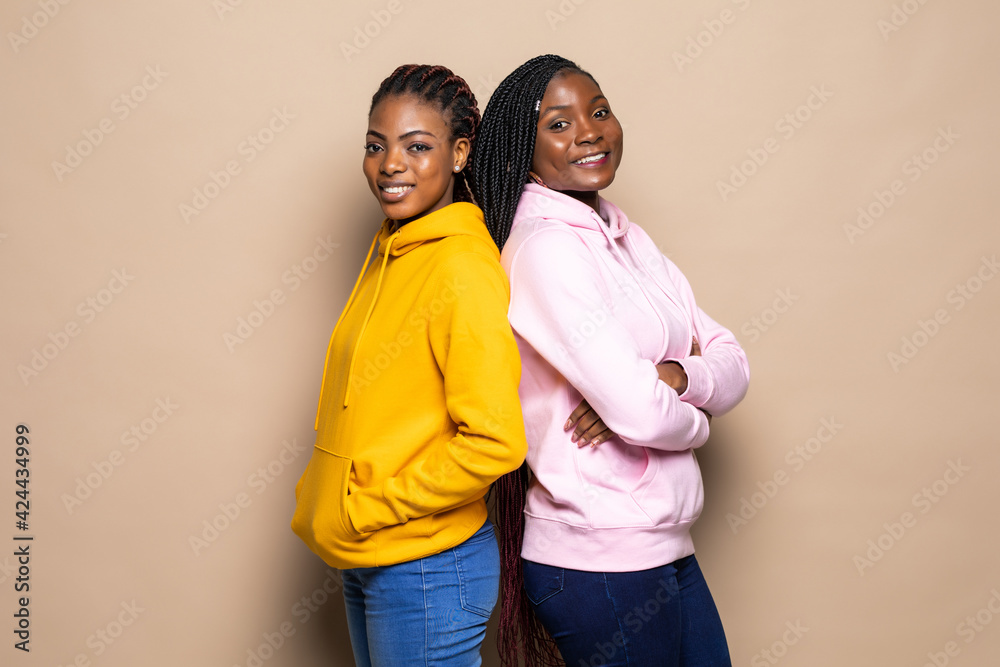 Obraz premium Portrait of two cheerful young women standing together isolated over beige background