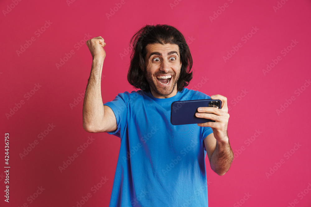 Excited brunette man in t-shirt playing online game on mobile phone Excited brunette man in t-shirt playing online game on mobile phone
