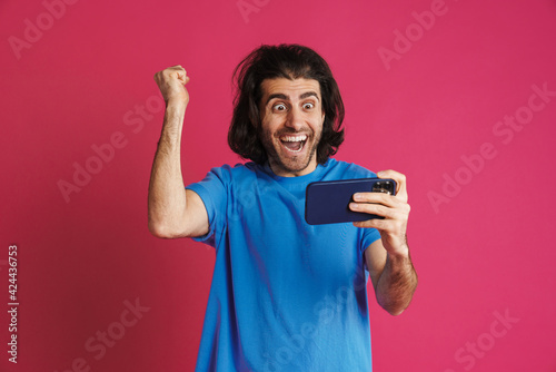 Excited brunette man in t-shirt playing online game on mobile phone