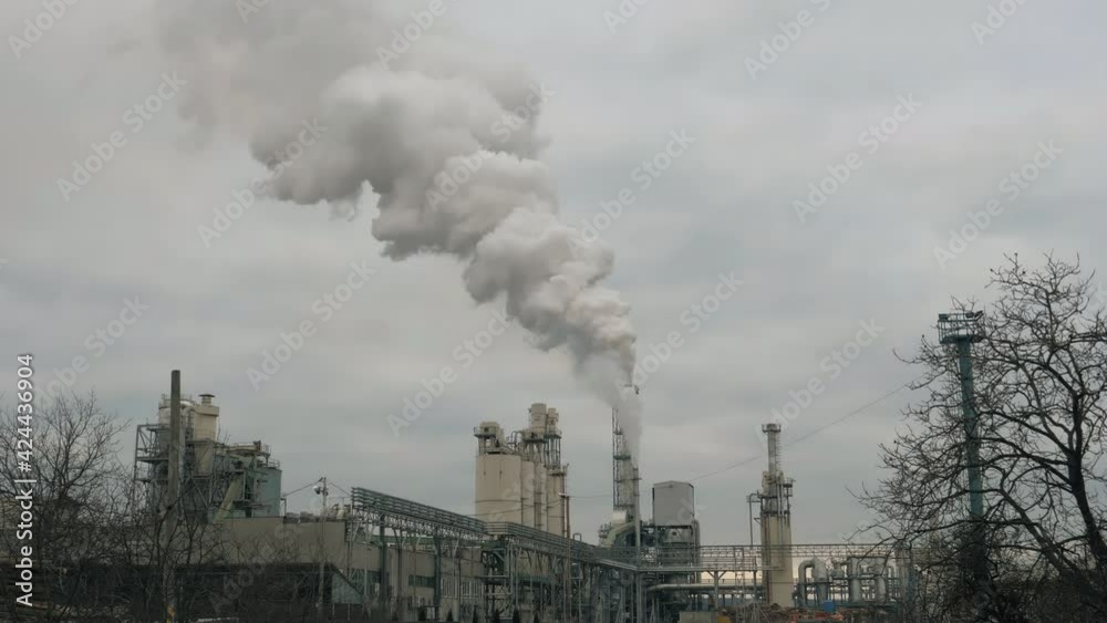 Smoke comes out of the factory chimney. Puffs of smoke coming out of a tall smokestack in a production facility. Environmental pollution problems. Smoke comes out of the factory chimney. Puffs of smoke coming out of a tall smokestack in a production facility. Environmental pollution problems.