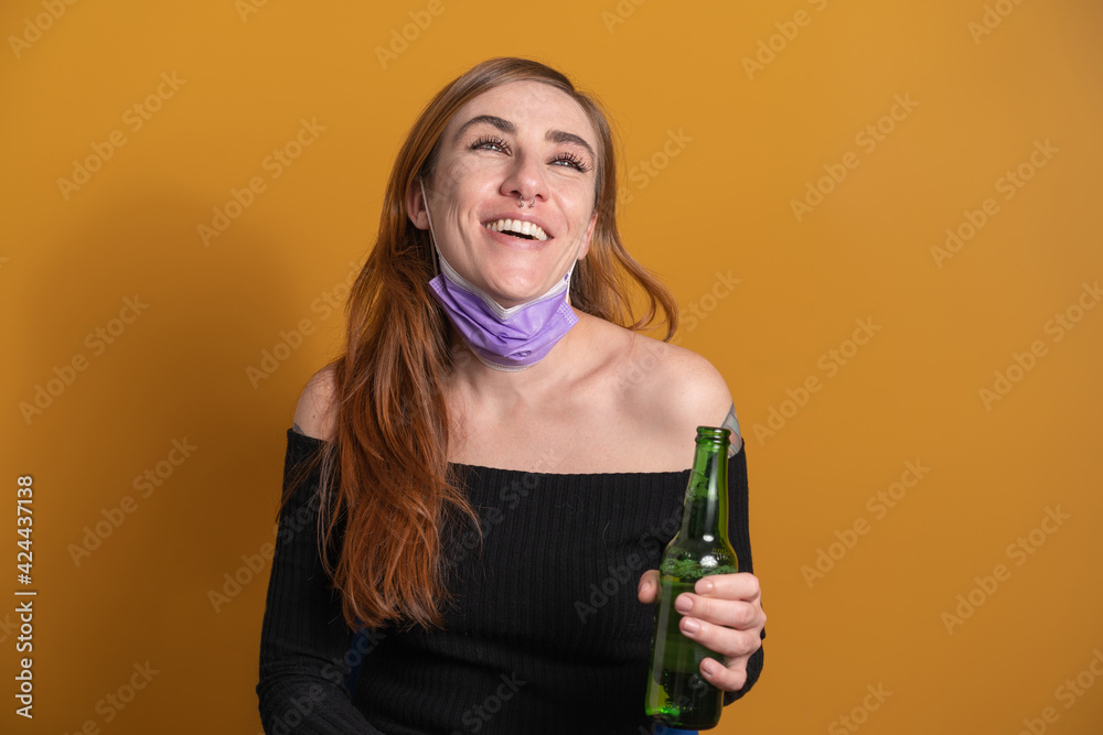 Young woman smiling and drinking a bottled beer isolated against an orange background Young woman smiling and drinking a bottled beer isolated against an orange background