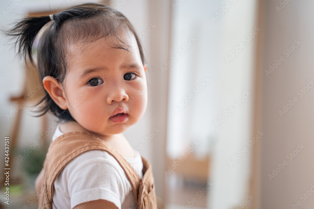portrait of asian baby infant in brown standing turn back looking at camera in living room at home on day time. baby response when calling. portrait of asian baby infant in brown standing turn back looking at camera in living room at home on day time. baby response when calling.