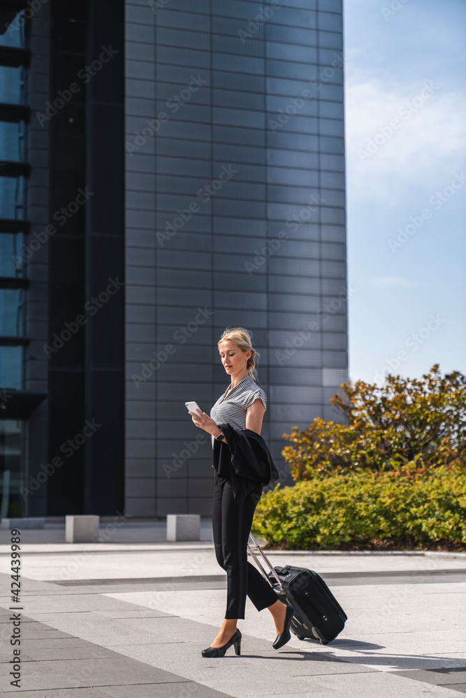 Mujer rubia ejecutiva caminando por centro de negocios con maleta en la mano