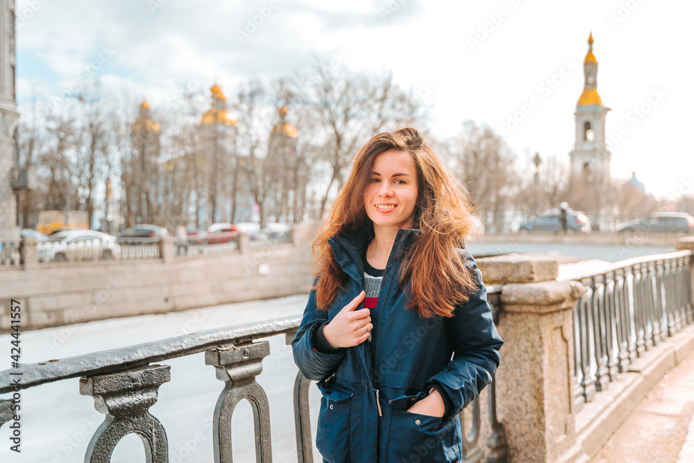 Fototapeta premium A young woman stands on the embankment of Saint Petersburg with a view of old buildings, early spring