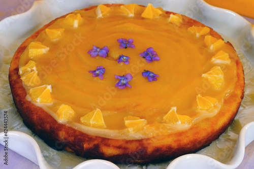 A round boiled Meyer lemon, almond and olive oil cake with sliced lemons and fresh violets on top