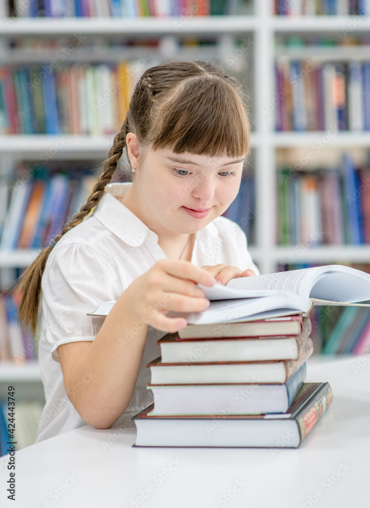 Girl with syndrome down reads a book at library. Education for disabled children concept Girl with syndrome down reads a book at library. Education for disabled children concept