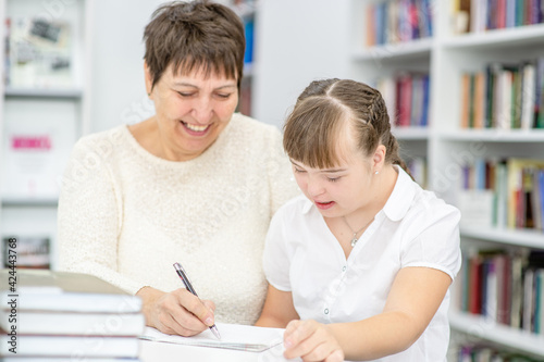 Smiling teacher and girl with syndrome doing homework together. Education for disabled children concept