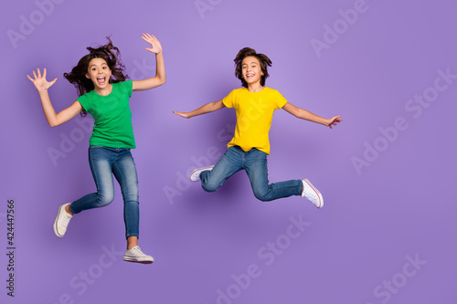 Full body photo of two young kids happy positive smile have fun jump up isolated over violet color background