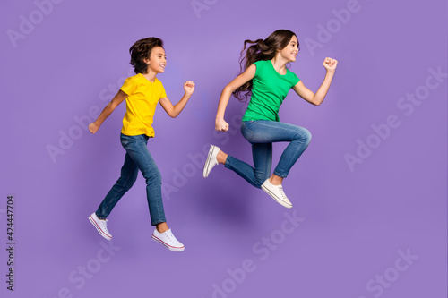 Full size profile side photo of two young kids happy smile go walk run jump hurry sale isolated over purple color background