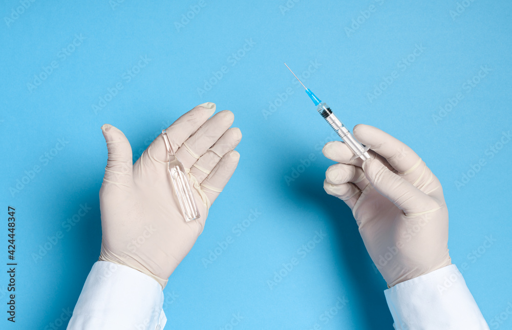 hands in medical gloves with a syringe on a blue background, imitation ...