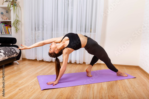Athletic girl doing yoga exercise in living room. Girl training at home, watching videos on laptop computer. Beautiful woman doing yoga. Young sporty woman practicing yoga. Woman working out indoors