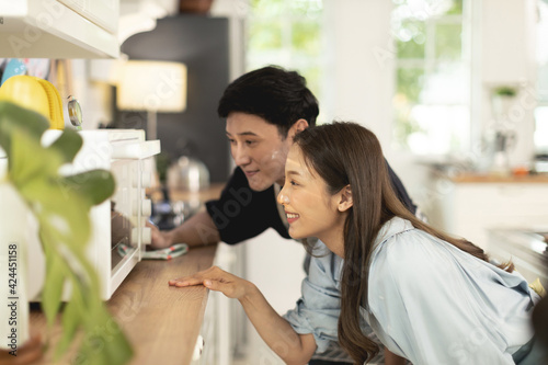 Asian couple Help each other to make a bakery In a romantic atmosphere in the kitchen at home. Young people are watching a cake made with an excited and happy face.